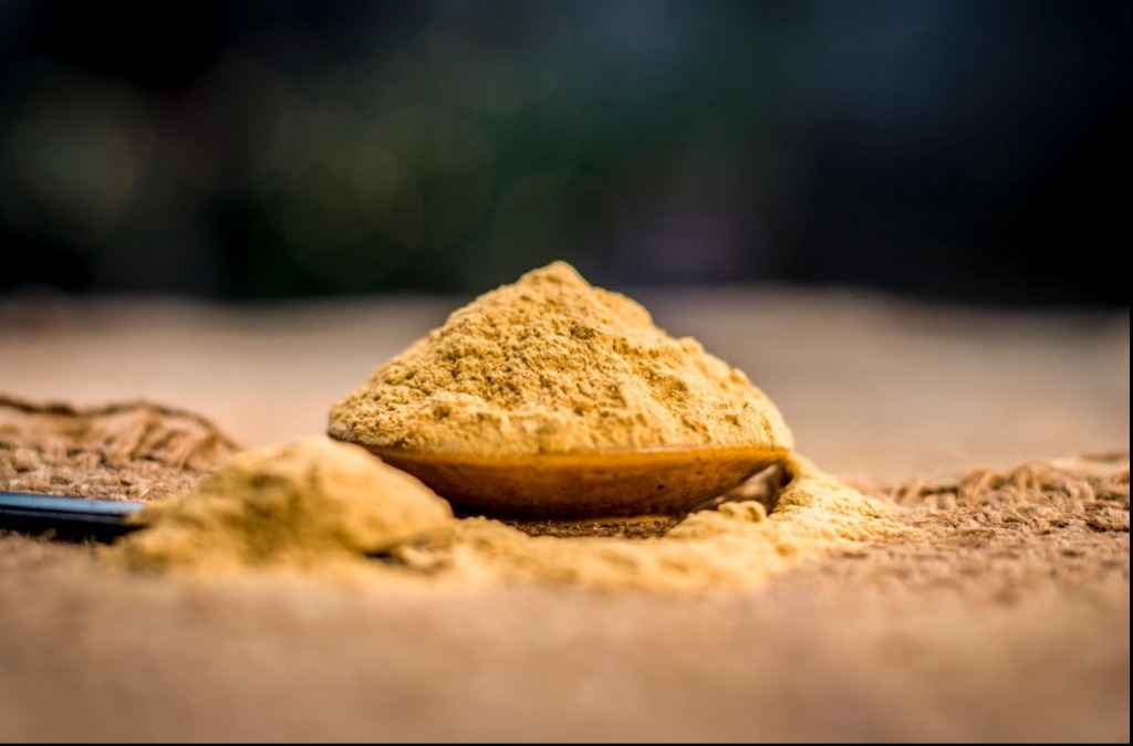 Artisanal bowls of finely ground ochre-colored clay powder with dried botanical leaves scattered around